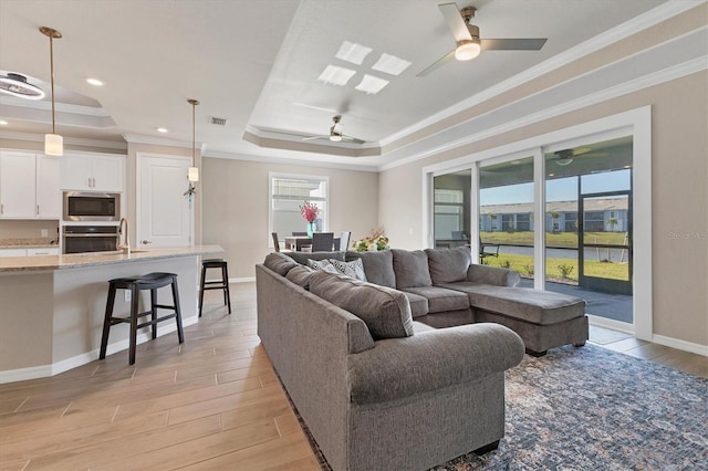 living room featuring plenty of natural light, a raised ceiling, and ornamental molding