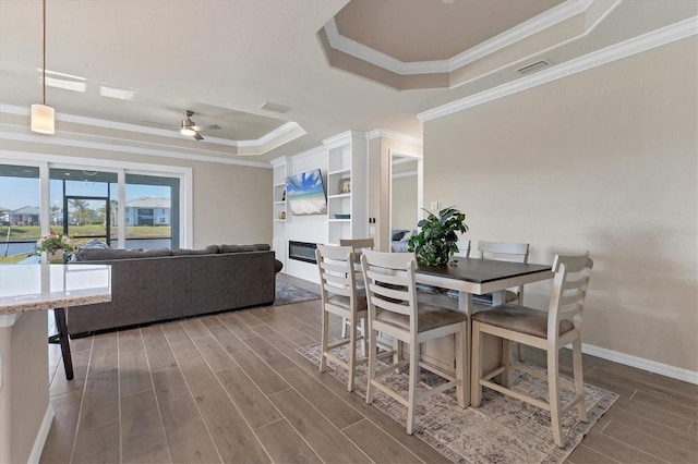 dining area with ceiling fan, a raised ceiling, built in features, crown molding, and a fireplace