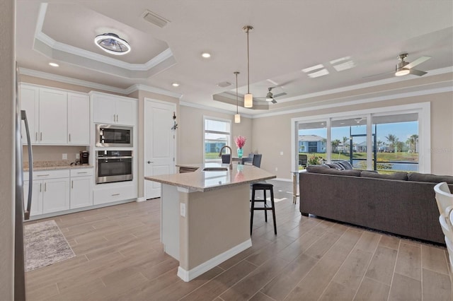 kitchen featuring stainless steel oven, a raised ceiling, pendant lighting, a center island with sink, and white cabinets