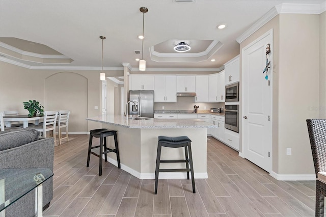 kitchen with white cabinets, decorative light fixtures, a raised ceiling, and an island with sink