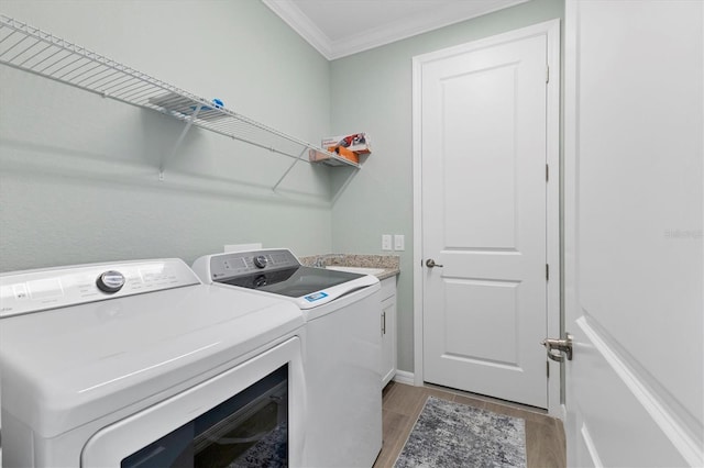 laundry area with crown molding, washer and clothes dryer, cabinets, and light hardwood / wood-style flooring