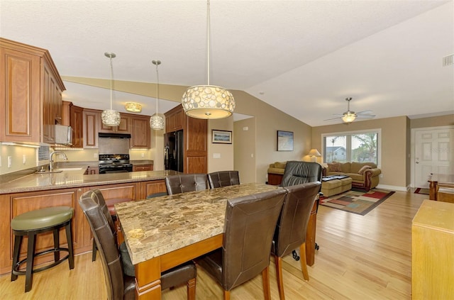 dining room with ceiling fan, sink, vaulted ceiling, and light wood-type flooring