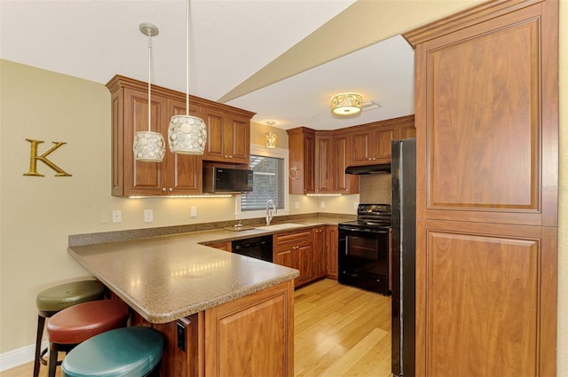 kitchen featuring kitchen peninsula, a breakfast bar, sink, black appliances, and decorative light fixtures