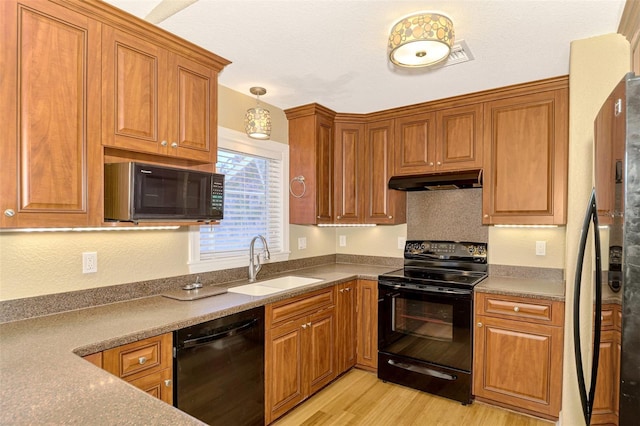 kitchen with black appliances, decorative light fixtures, light wood-type flooring, and sink