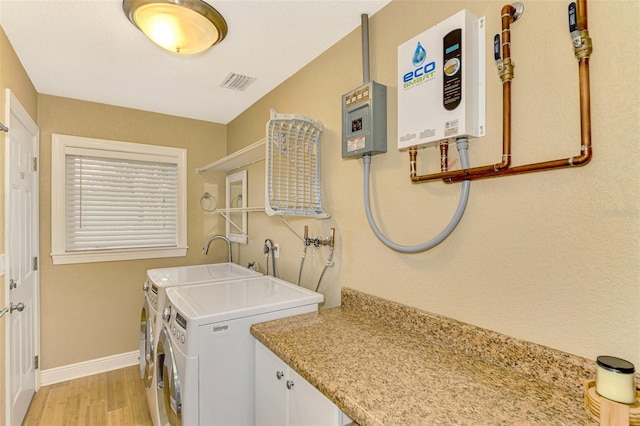 washroom with cabinets, sink, washer and dryer, light wood-type flooring, and water heater