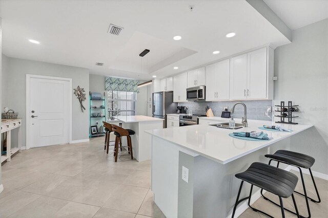 kitchen with sink, stainless steel appliances, a kitchen breakfast bar, decorative light fixtures, and white cabinets