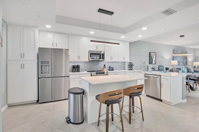 kitchen with pendant lighting, a raised ceiling, white cabinets, and appliances with stainless steel finishes