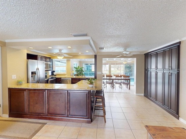 kitchen with kitchen peninsula, a kitchen bar, stainless steel appliances, and crown molding