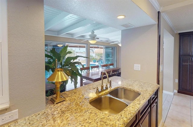 kitchen with light stone countertops, sink, ceiling fan, light tile patterned floors, and ornamental molding