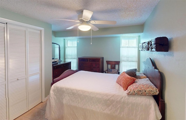 bedroom with ceiling fan, light tile patterned floors, a textured ceiling, and a closet