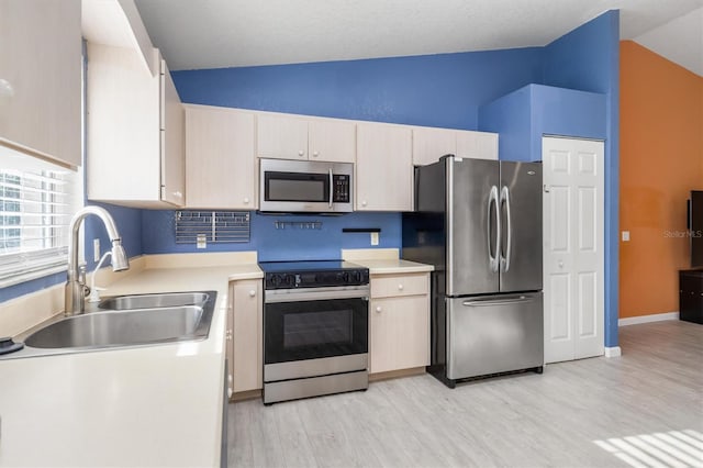 kitchen with sink, a textured ceiling, vaulted ceiling, appliances with stainless steel finishes, and light wood-type flooring