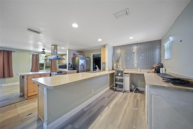 kitchen featuring island exhaust hood, kitchen peninsula, stainless steel appliances, sink, and light hardwood / wood-style floors