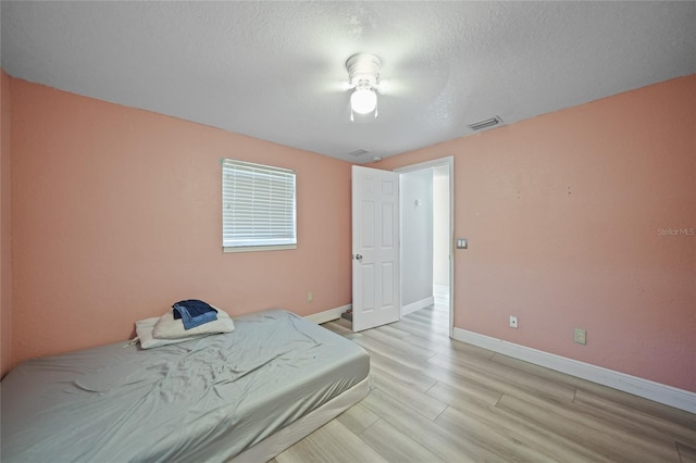 bedroom featuring ceiling fan, light wood-type flooring, and a textured ceiling