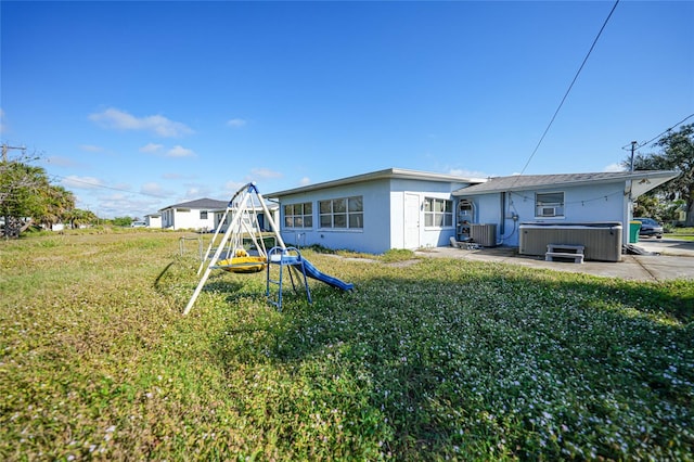 rear view of property featuring a playground, a patio area, a yard, and a hot tub