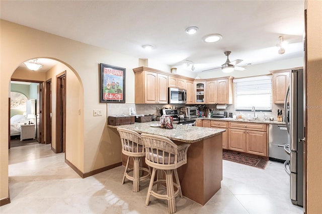 kitchen featuring kitchen peninsula, backsplash, a breakfast bar, stainless steel appliances, and ceiling fan