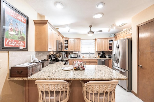 kitchen featuring ceiling fan, light stone countertops, appliances with stainless steel finishes, kitchen peninsula, and a breakfast bar area