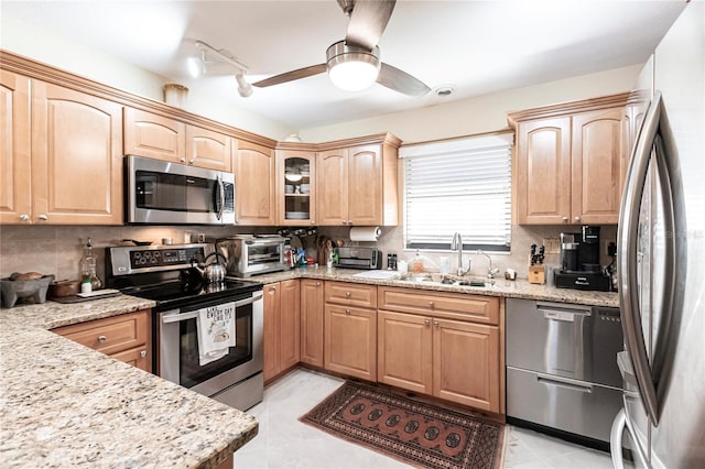 kitchen with light stone countertops, sink, ceiling fan, stainless steel appliances, and backsplash