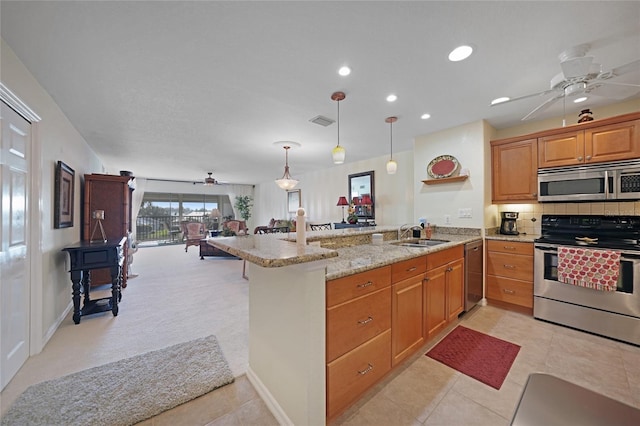 kitchen with kitchen peninsula, sink, hanging light fixtures, appliances with stainless steel finishes, and light stone counters