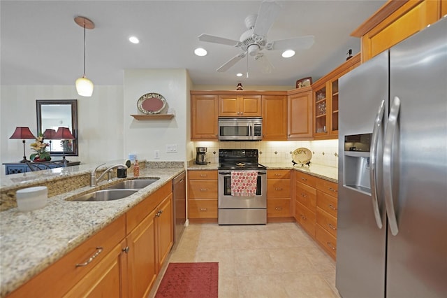 kitchen featuring stainless steel appliances, ceiling fan, sink, hanging light fixtures, and light stone counters