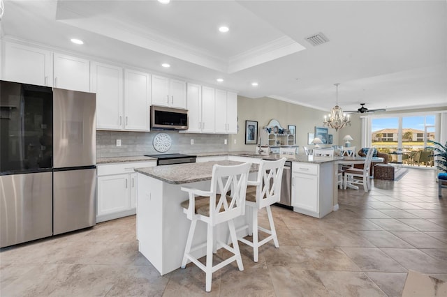 kitchen with hanging light fixtures, a raised ceiling, kitchen peninsula, a kitchen island, and appliances with stainless steel finishes