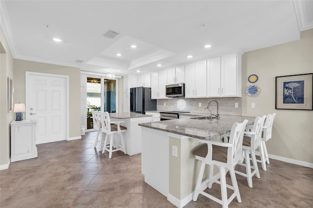 kitchen featuring kitchen peninsula, appliances with stainless steel finishes, light stone countertops, a breakfast bar, and a raised ceiling