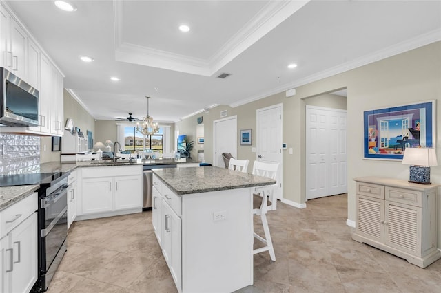 kitchen featuring kitchen peninsula, a breakfast bar, stainless steel appliances, a center island, and white cabinetry