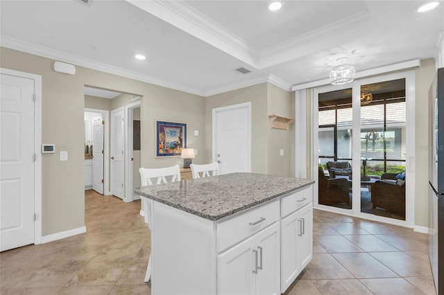 kitchen featuring light stone counters, a tray ceiling, crown molding, white cabinets, and a kitchen island