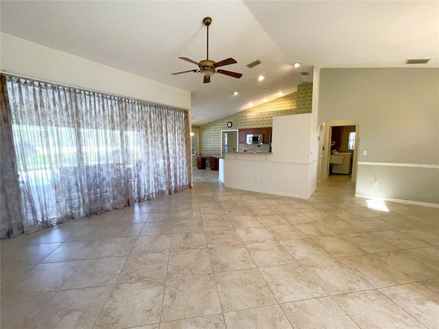 unfurnished living room featuring ceiling fan, light tile patterned flooring, brick wall, and lofted ceiling