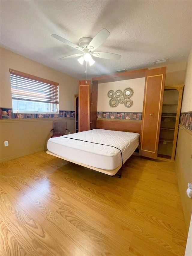 bedroom featuring ceiling fan, light hardwood / wood-style flooring, and a textured ceiling