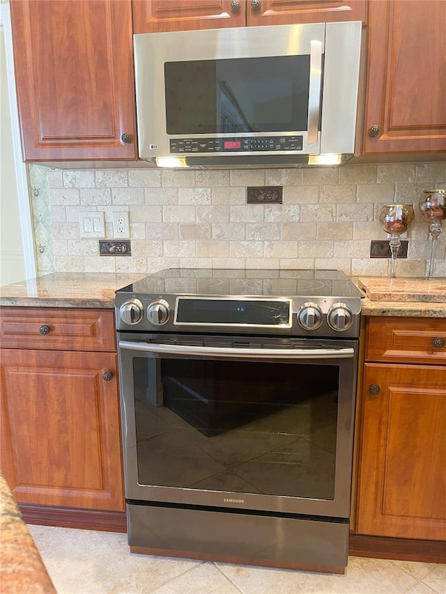 kitchen with light stone countertops, appliances with stainless steel finishes, backsplash, and light tile patterned floors