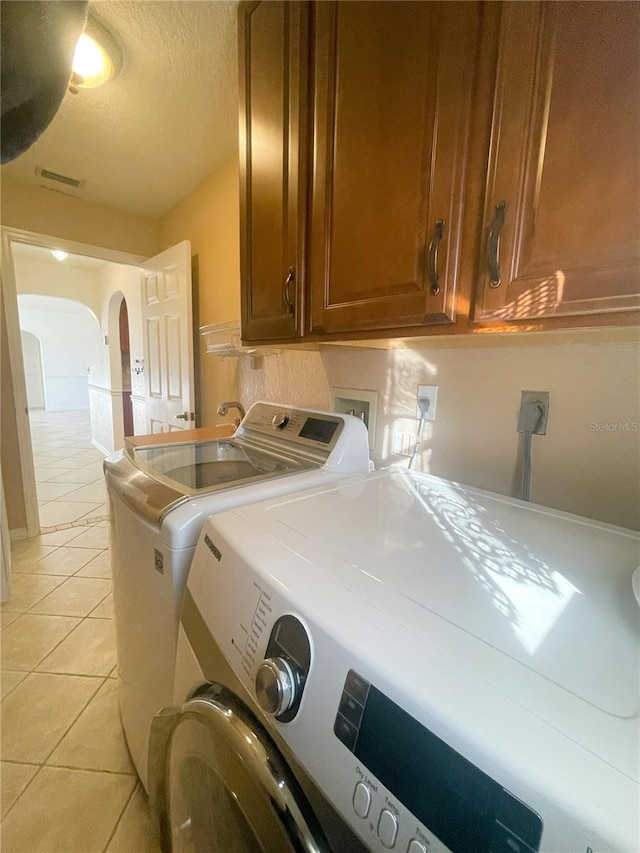 laundry area with washer and clothes dryer, cabinets, light tile patterned floors, and a textured ceiling