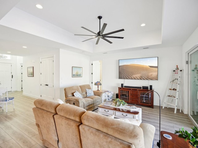 living room featuring a raised ceiling, ceiling fan, and light wood-type flooring