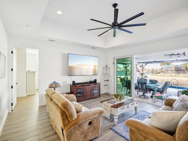 living room with light wood-type flooring, a tray ceiling, and ceiling fan