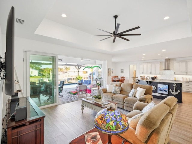 living room with ceiling fan, light hardwood / wood-style floors, and a tray ceiling