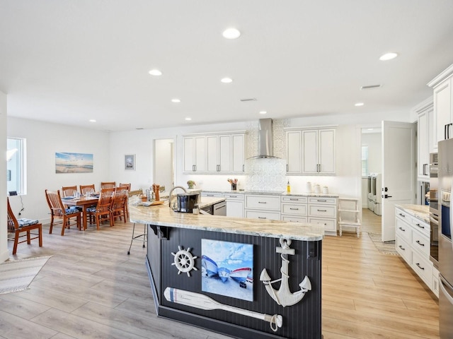 kitchen featuring a breakfast bar area, white cabinetry, light hardwood / wood-style flooring, and wall chimney exhaust hood