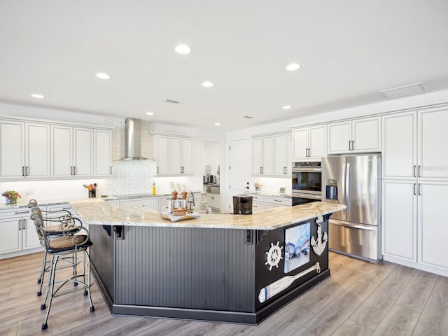 kitchen featuring a large island, wall chimney exhaust hood, white cabinets, and stainless steel appliances