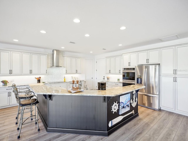 kitchen featuring white cabinetry, a large island, wall chimney exhaust hood, and appliances with stainless steel finishes