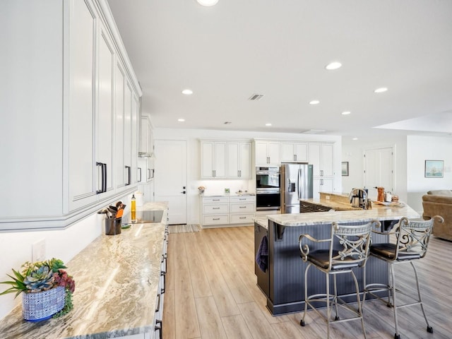 kitchen featuring a large island with sink, light stone counters, white cabinets, and stainless steel appliances