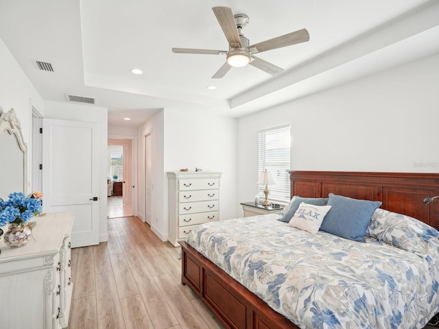 bedroom featuring a tray ceiling, multiple windows, ceiling fan, and light hardwood / wood-style floors