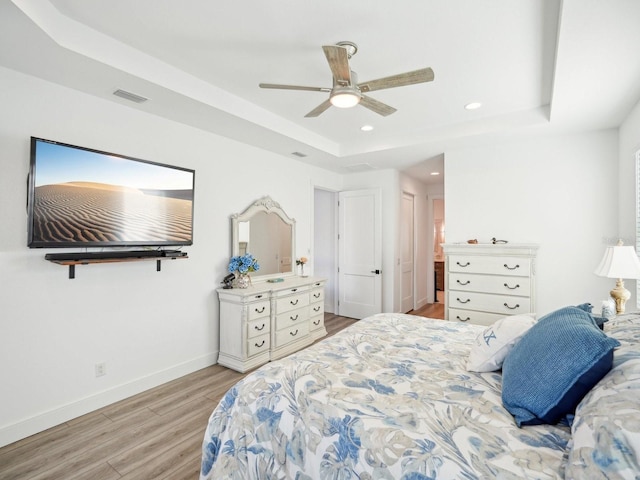 bedroom with light wood-type flooring, a raised ceiling, and ceiling fan