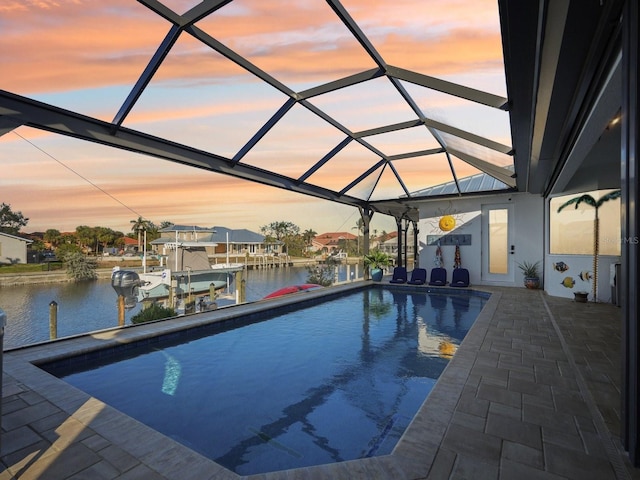 pool at dusk featuring a boat dock, a patio area, a water view, and glass enclosure