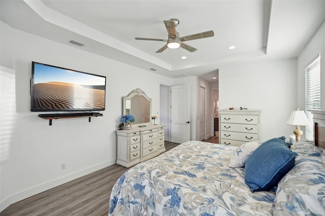 bedroom featuring visible vents, baseboards, a tray ceiling, recessed lighting, and wood finished floors