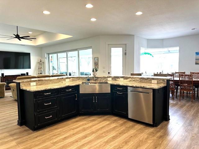 kitchen with dark cabinetry, a sink, open floor plan, dishwasher, and light wood-type flooring