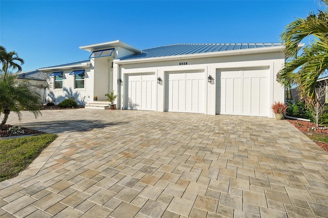 prairie-style home featuring stucco siding, a standing seam roof, decorative driveway, metal roof, and a garage