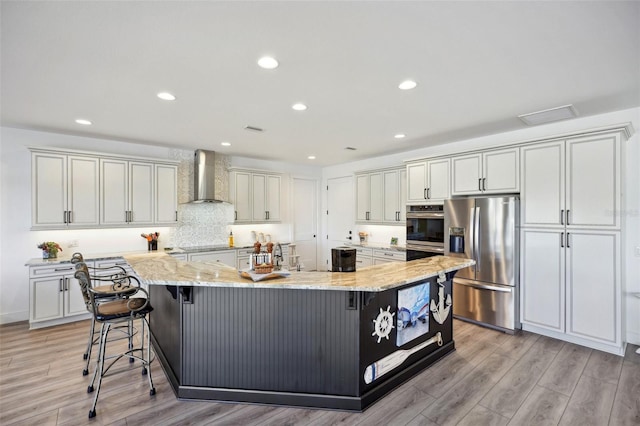 kitchen featuring light wood-style flooring, light stone countertops, appliances with stainless steel finishes, and wall chimney exhaust hood