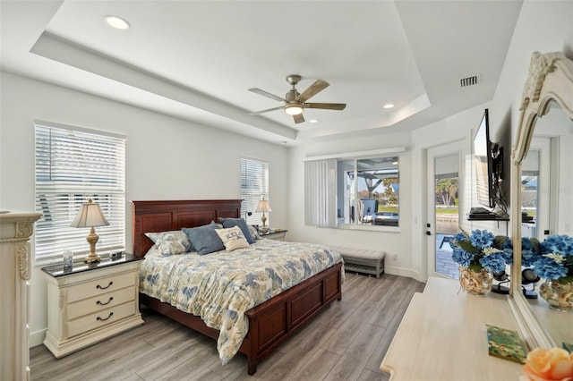 bedroom featuring light wood finished floors, visible vents, recessed lighting, a raised ceiling, and access to outside