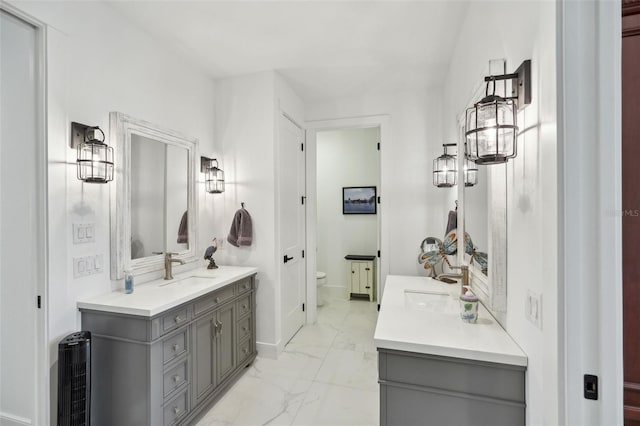 full bathroom featuring marble finish floor, toilet, two vanities, and a sink