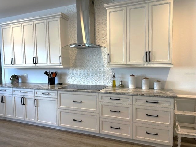 kitchen with black electric stovetop, wall chimney exhaust hood, white cabinets, and light stone counters