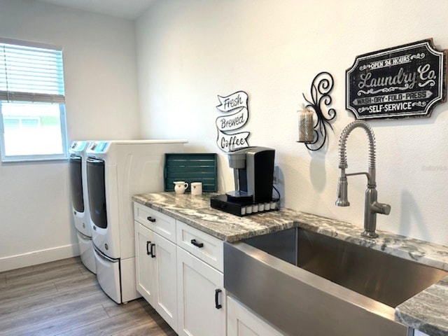 washroom with light wood-style flooring, a sink, washing machine and dryer, cabinet space, and baseboards