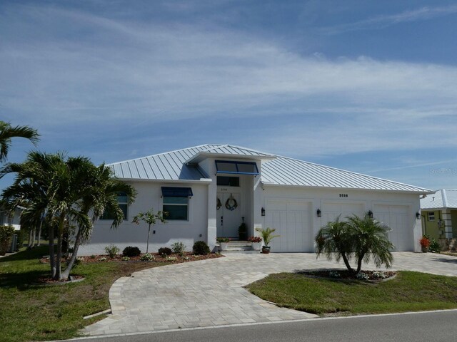 ranch-style home with metal roof, stucco siding, a standing seam roof, decorative driveway, and a garage